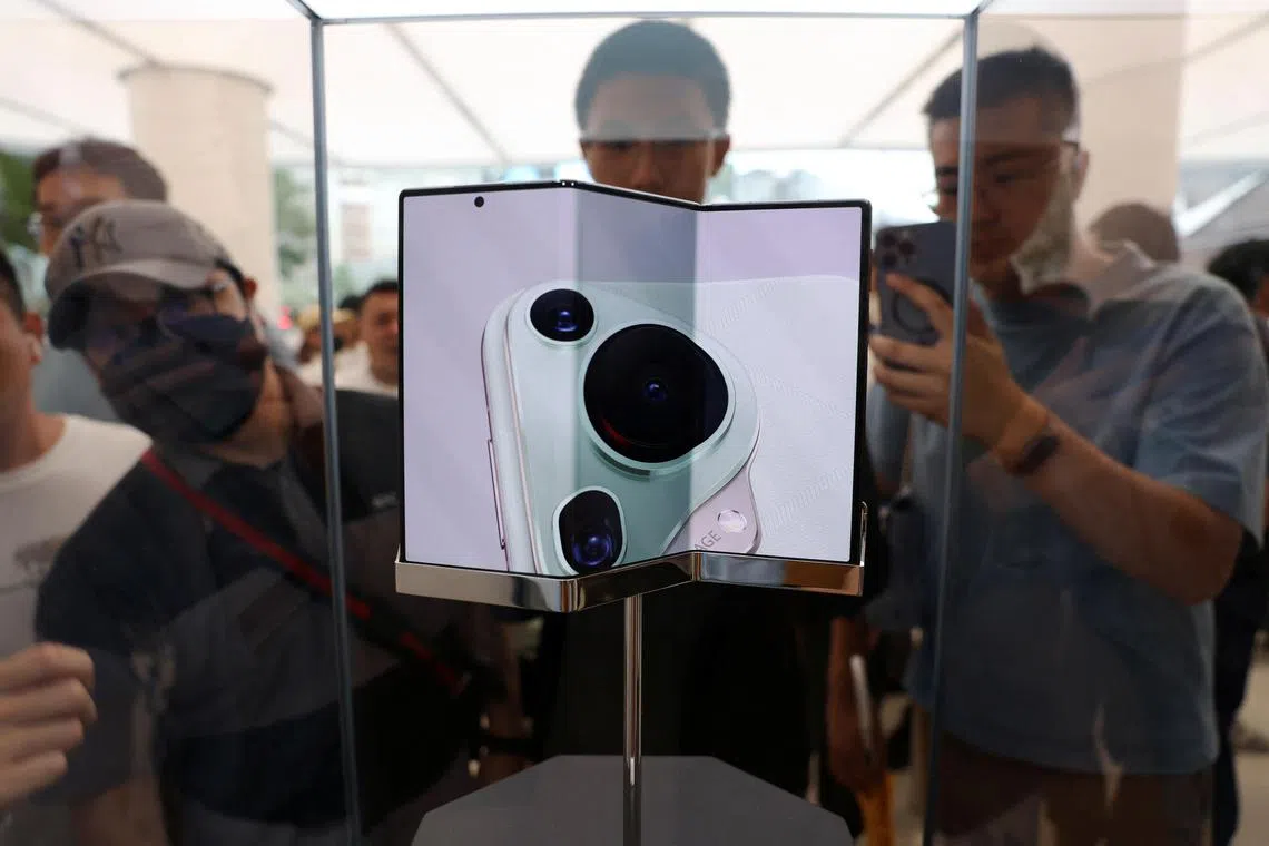 People look at Huawei's new tri-foldable smartphone Mate XT displayed in a glass case at a Huawei flagship store in Beijing, China September 10, 2024. REUTERS/Florence Lo