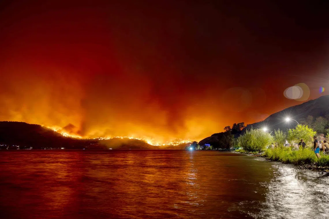 (FILES) Residents watch the McDougall Creek wildfire in West Kelowna, British Columbia, Canada, on August 17, 2023, from Kelowna. Human-caused climate change made 2023's severe, months-long "fire weather" conditions that drove Canada's record-breaking blazes at least seven times more likely to happen, according to a new scientific analysis published on August 22, 2023. The study by the World Weather Attribution group also found that over the year, fire-prone conditions were 50 percent more intense as a result of global warming, primarily a result of burning fossil fuels. (Photo by Darren HULL / AFP)