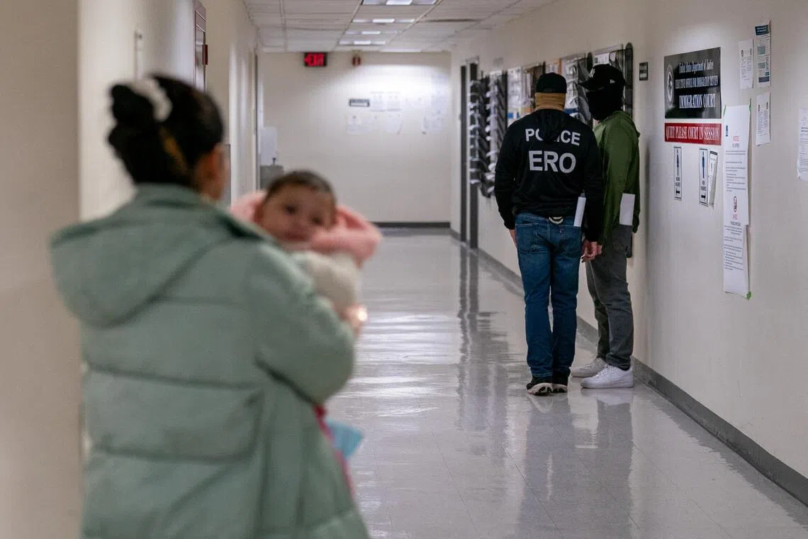 A woman carrying a child walks toward Immigration and Customs Enforcement (ICE) agents in the hallway of the U.S. immigration court in Manhattan, New York City, on Dec 18, 2025