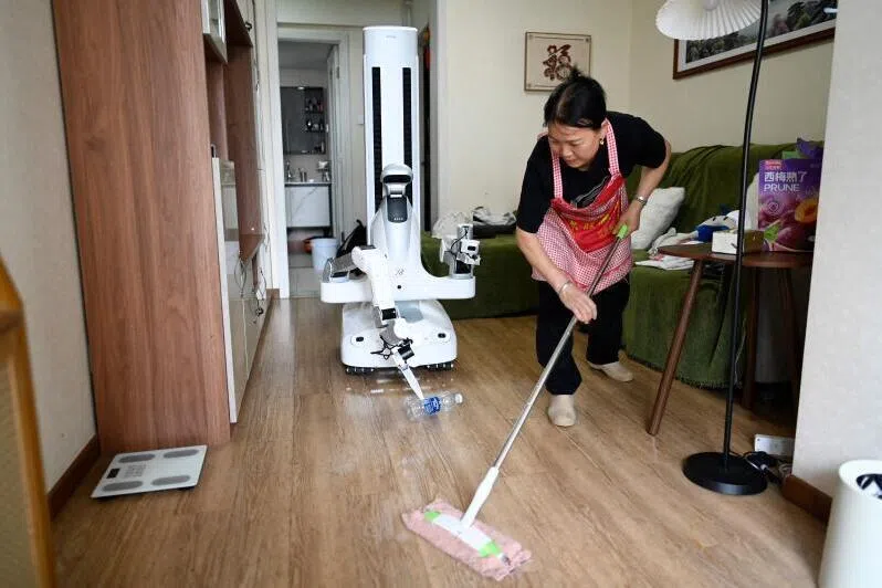 An X Square robot carrying a bottle to a rubbish bin as a housekeeper cleans the floor at a customer’s home in Beijing.