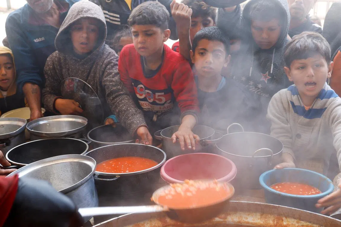 Palestinian children wait to receive food cooked by a charity kitchen, during the Muslim holy month of Ramadan, in Khan Younis, in the southern Gaza Strip, March 9, 2025. REUTERS/Hatem Khaled