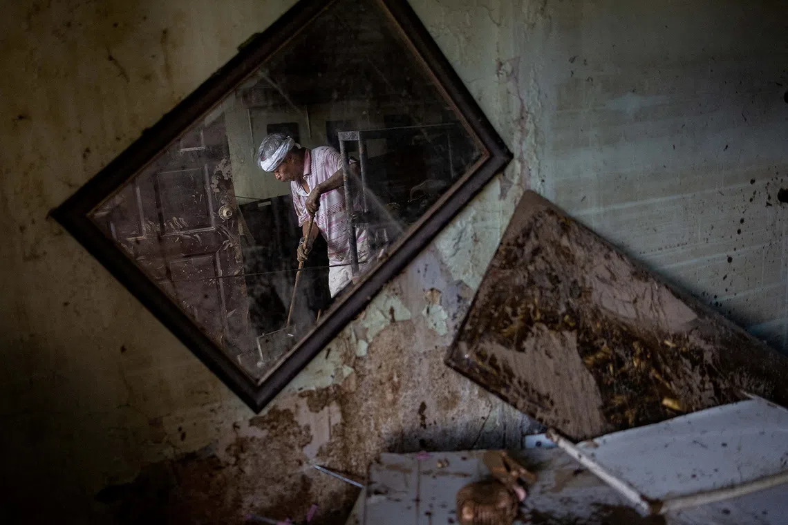 Eusebio Cuyos, 75, is reflected in a mirror as he sweeps mud out of his home after heavy flooding brought on by Typhoon Kalmaegi in Bacayan, Cebu City, Philippines, on Nov 5, 2025. 