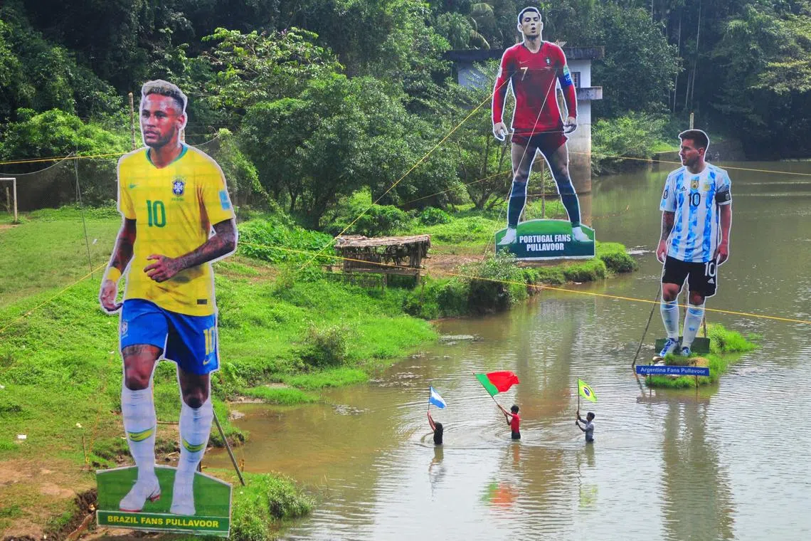 Fans wave flags next to the giant cutouts of players from Brazil's Neymar (L), Portuguese Cristiano Ronaldo (C) and Argentine Lionel Messi, erected by football fans in river Cherupuzha at Kozhikode in India's Kerala state on November 7, 2022, ahead of the Qatar 2022 FIFA World Cup football tournament.
