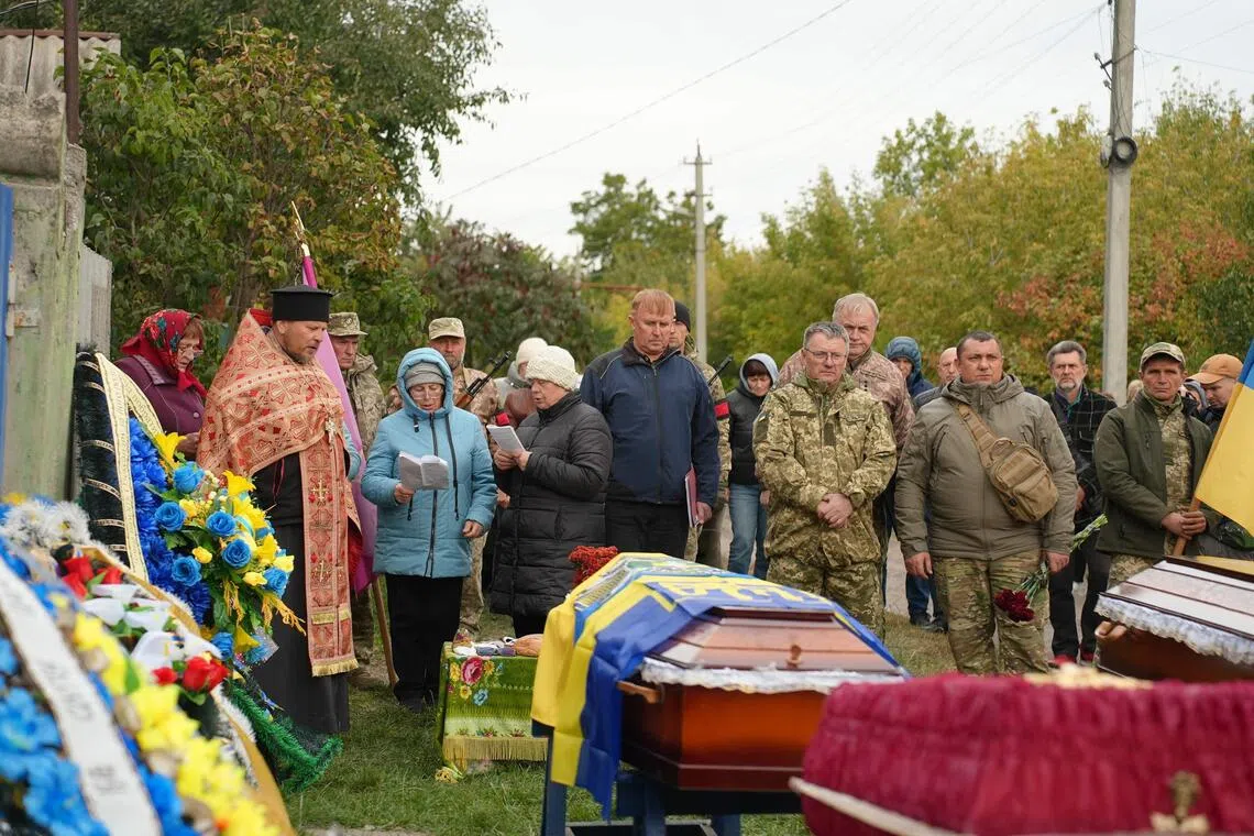 Relatives and friends mourn over coffins during a funeral ceremony for a family killed following a Russian drone strike in the Sumy oblast in Chernechchyna, on Oct 1, 2025.