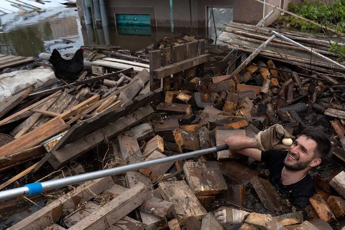 An animal rescue volunteer (right) is watched by a chicken as he holds an egg while he swims among debris in floodwaters at Kherson, Ukraine, on June 8, after the city was engulfed by rising water levels following damage sustained at Kakhovka hydroelectric power plant dam. 