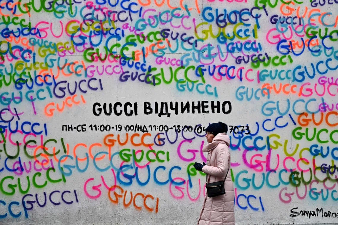 A woman walks past the Gucci fashion house shop window covered with protective chipboard against fragments of shelling with a sign reading, "Gucci is open", in the center of Ukrainian capital of Kyiv on Dec 12, 2022.