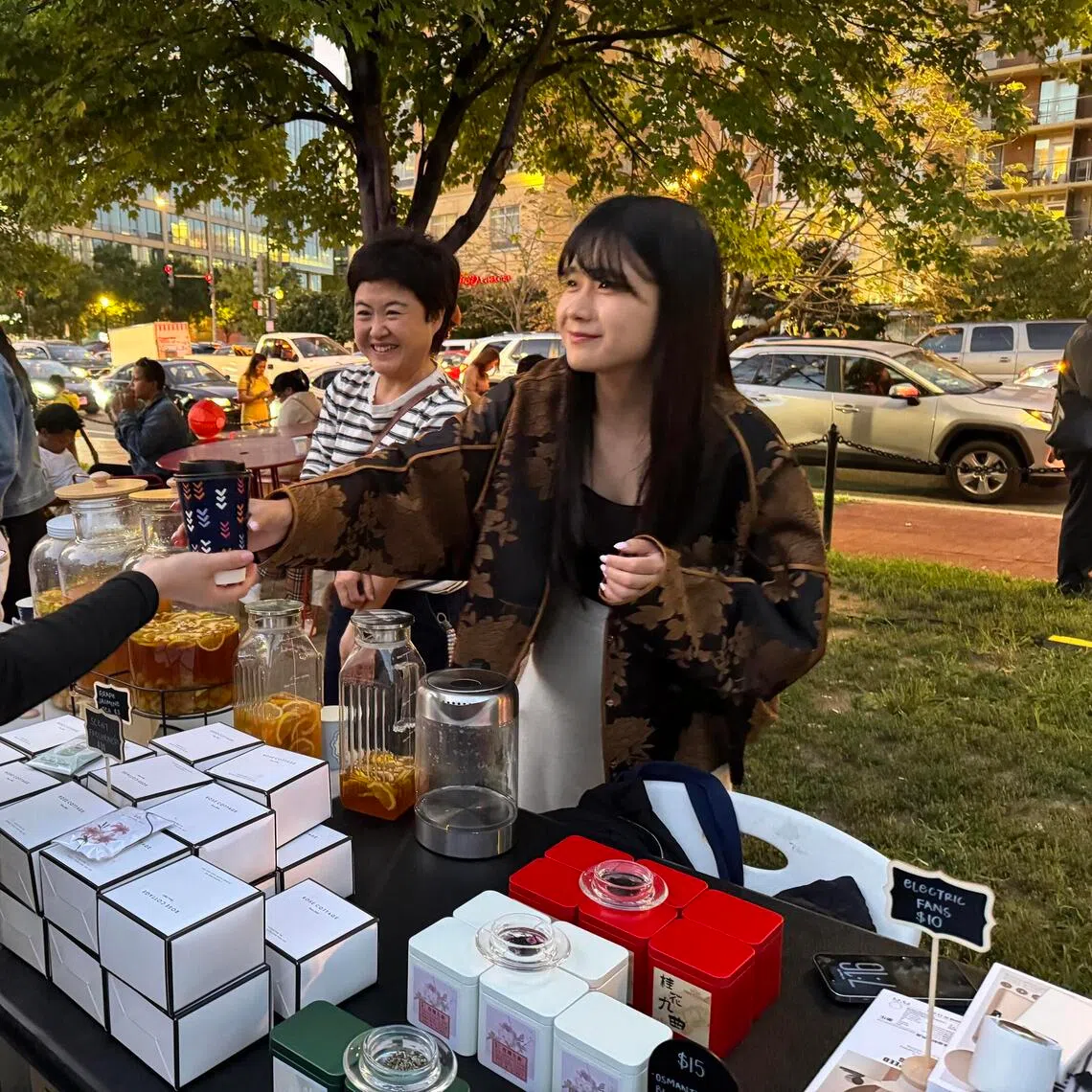 Zhu Simin (right), who was born in China and moved to the US, tending to her Chinese tea booth at the Mid-Autumn Festival night market at Washington, DC’s Chinatown Park in September.
