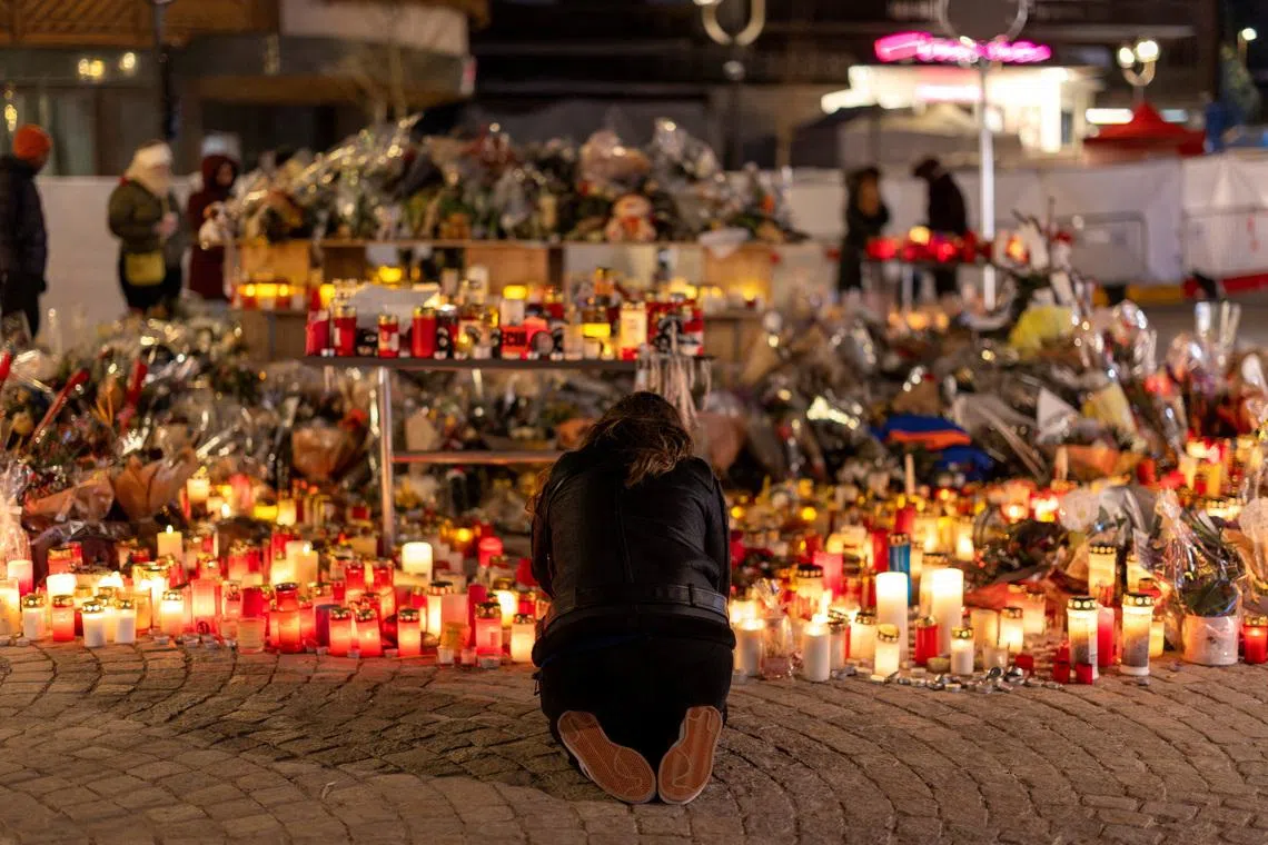 A woman lights a candle at a makeshift memorial outside the \"Le Constellation\" bar, after a deadly fire and explosion during a New Year's Eve party, in the upscale ski resort of Crans-Montana in southwestern Switzerland, January 5, 2026. REUTERS/Umit Bektas