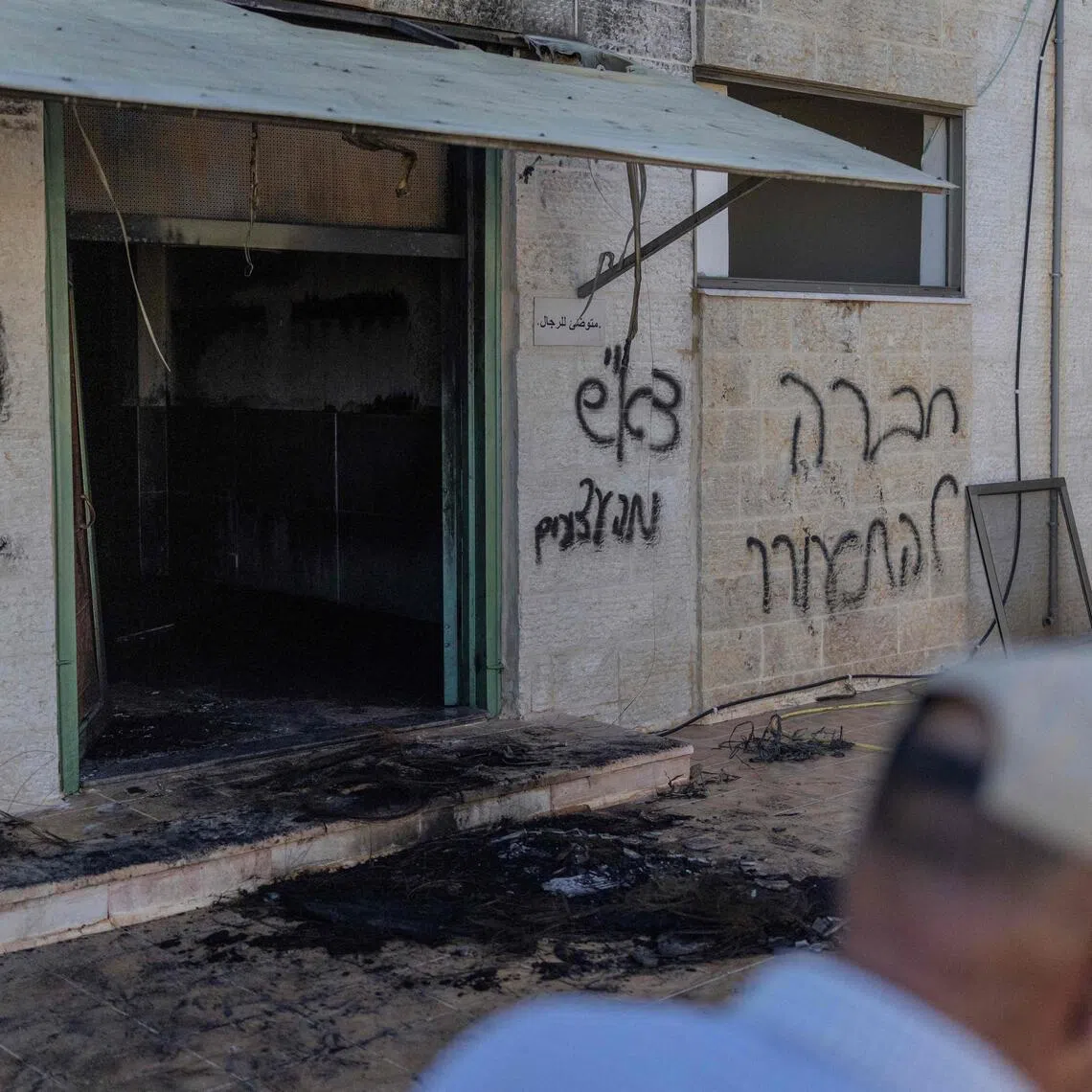 A Palestinian man walks past the damage mosque reportedly burnt by Israeli settlers overnight, with one of the Hebrew graffiti reading "nekama" or "revenge" daubed on the wall.