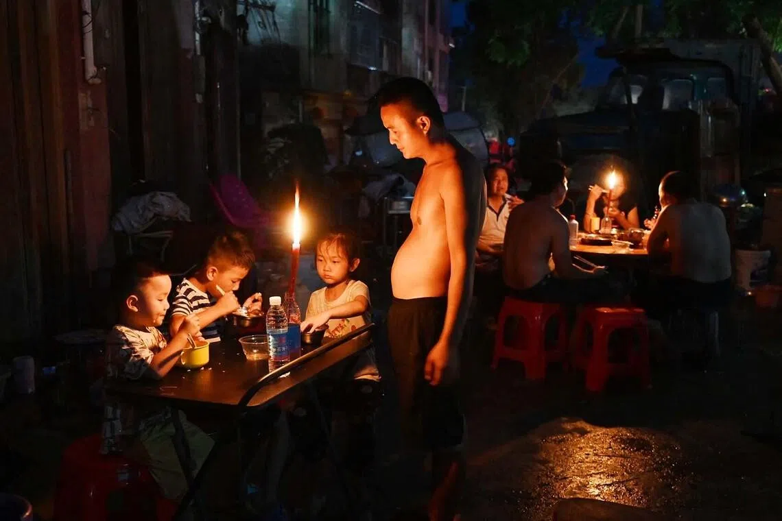 TOPSHOT - A father looks on as children have dinner by candlelight outside a house in Gantang after electricity was knocked out by floodwaters from a collapsed reservoir in China’s southwest Guangxi region on July 9, 2026. The death toll from devastating floods in southern China's Guangxi region rose to 39 on July 9, with nine people still missing, state media reported, as residents went about cleaning up. (Photo by GREG BAKER / AFP)