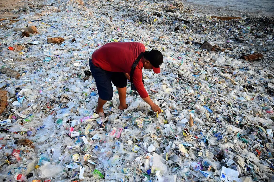 TOPSHOT - A man looks through plastic and other debris washed ashore at Kedonganan Beach near Denpasar on Indonesia's resort island of Bali on March 19, 2024. (Photo by SONNY TUMBELAKA / AFP)