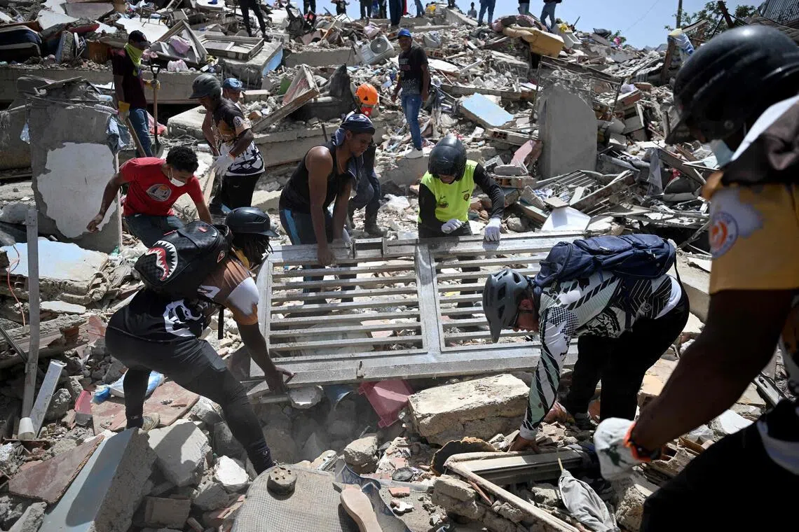 TOPSHOT - Volunteers lift a metal gate as they search through debris on the rubble of collapsed buildings in Catia La Mar, La Guaira, Venezuela, on June 26, 2026, following deadly earthquakes. The death toll from two powerful earthquakes that devastated Venezuela earlier this week rose to 920 on June 26, National Assembly President Jorge Rodriguez said. (Photo by Federico PARRA / AFP)