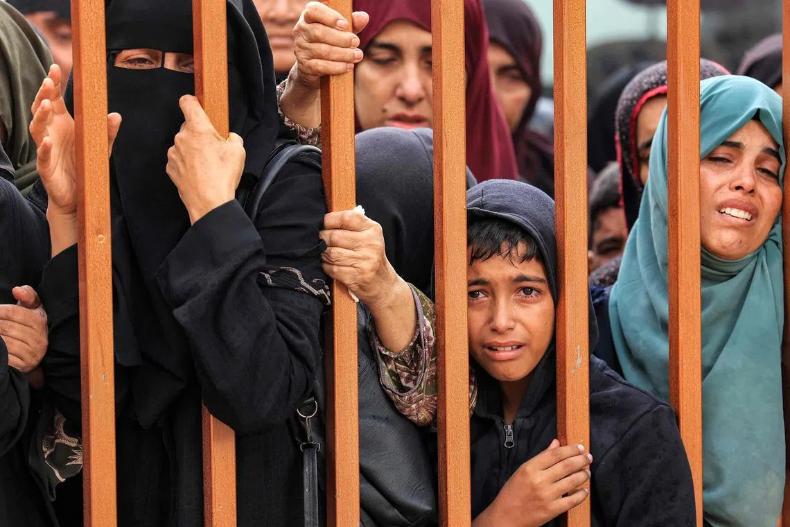 People mourn as they stand behind a metal fence, near the bodies of victims who were killed in Israeli bombardments, outside the morgue at Nasser hospital in Khan Younis, in the southern Gaza Strip.