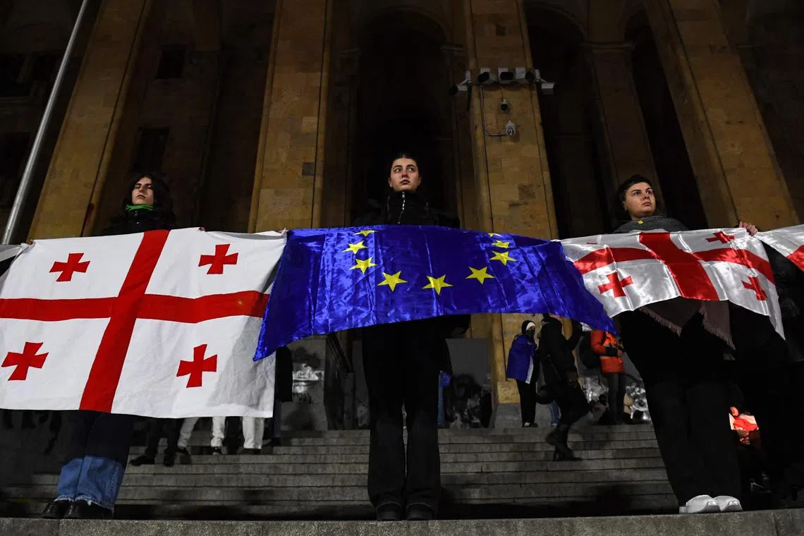 Anti-government protesters with flags of Georgia and European Union rally in front of the parliament during an eighth consecutive day of mass demonstrations against the government's postponement of EU accession talks until 2028, in central Tbilisi on December 5, 2024. (Photo by KAREN MINASYAN / AFP)