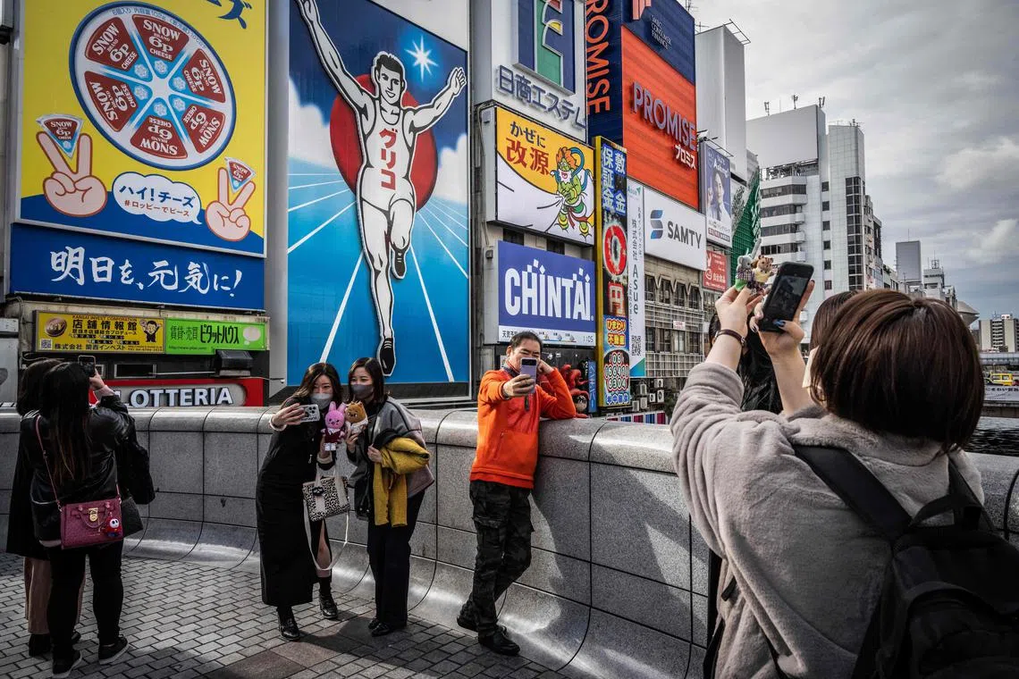 People take photographs in front of the Dotonbori Glico Sign in Osaka on December 1, 2022. (Photo by Yuichi YAMAZAKI / AFP)