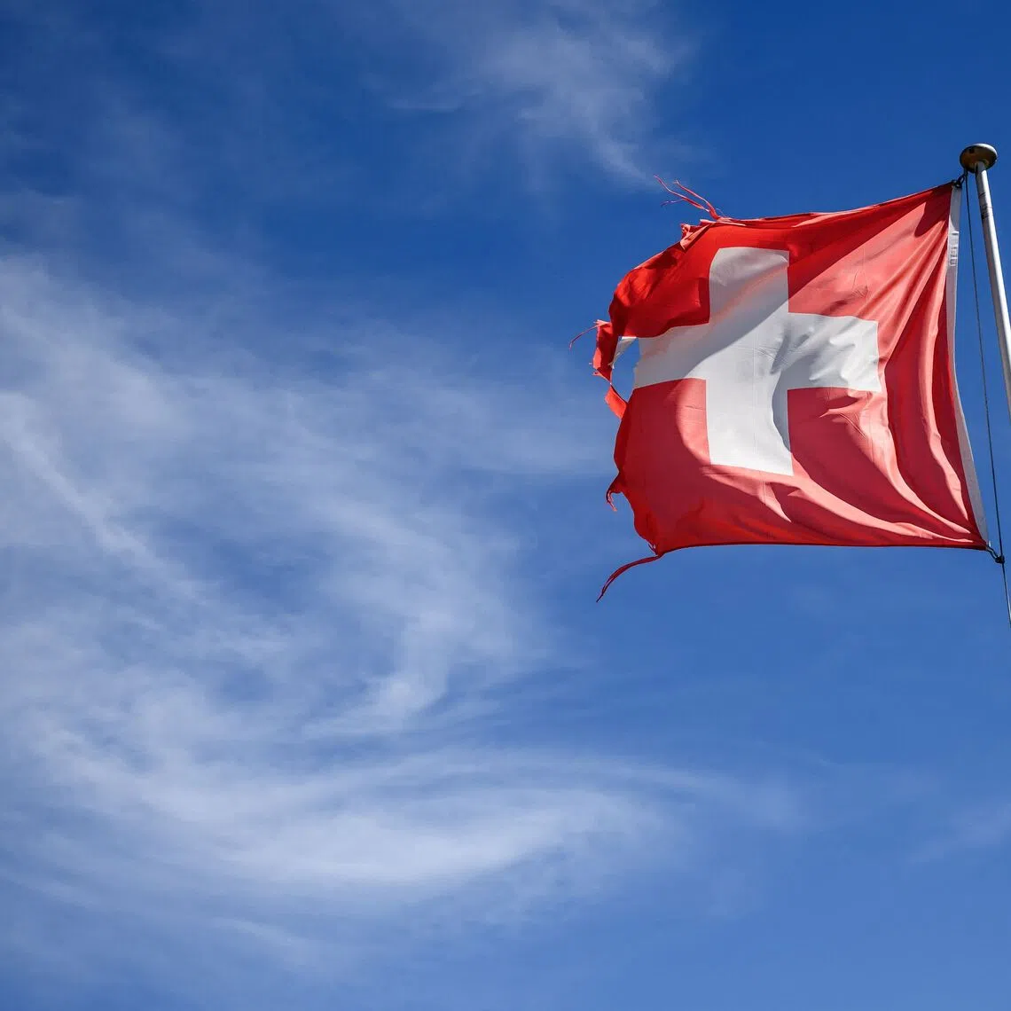 A worn Swiss flag flutters in the breeze above Crans-Montana, Switzerland on September 1, 2026. (Photo by Fabrice COFFRINI / AFP)