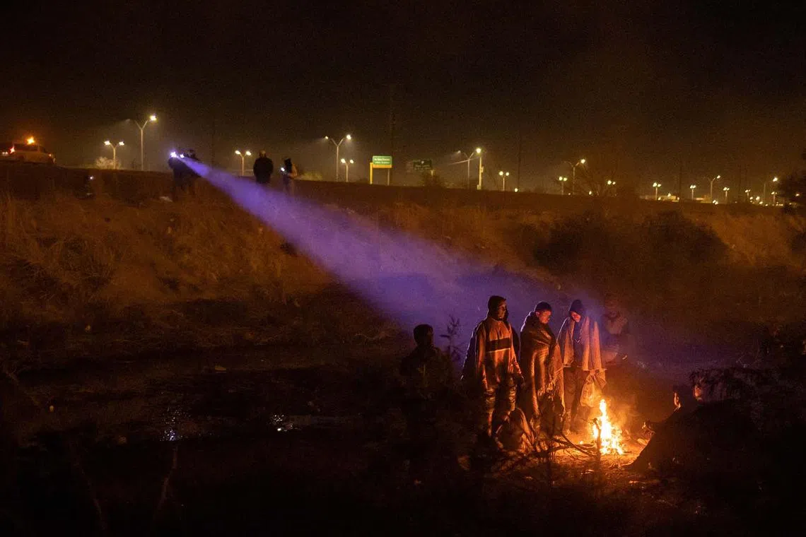 Officials with the National Institute of Migration shining their flashlights from Ciudad Juarez, Mexico, towards migrants taking refuge along the dry riverbed of the Rio Grande river as they gathered around a fire while searching for an entry point into the United States, as seen from El Paso, Texas, US, April 2, 2024. 