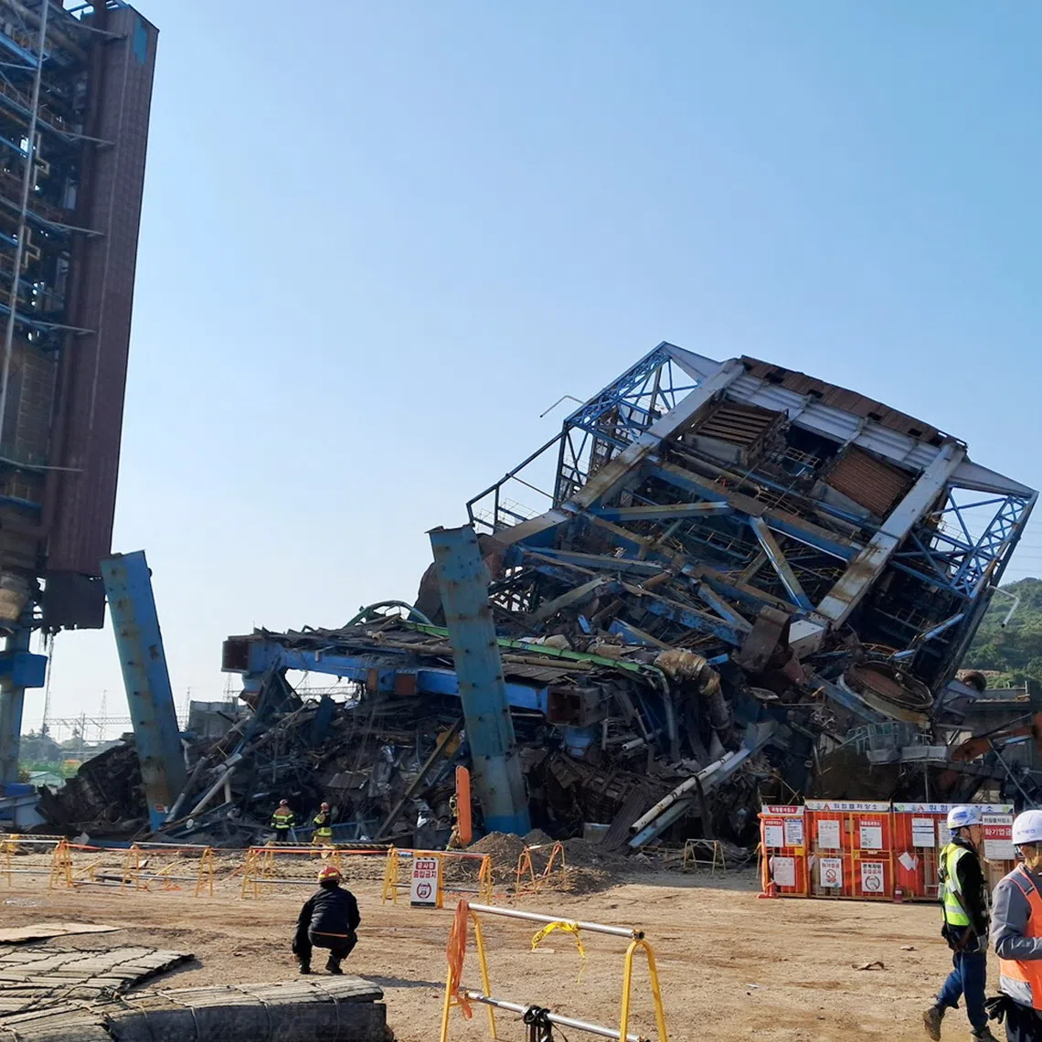 People walk near a large structure which collapsed and where multiple people are believed to be trapped, at the Korea East-West Power's Ulsan Power Plant headquarters, in Ulsan, South Korea, November 6, 2025.     Yonhap/via REUTERS