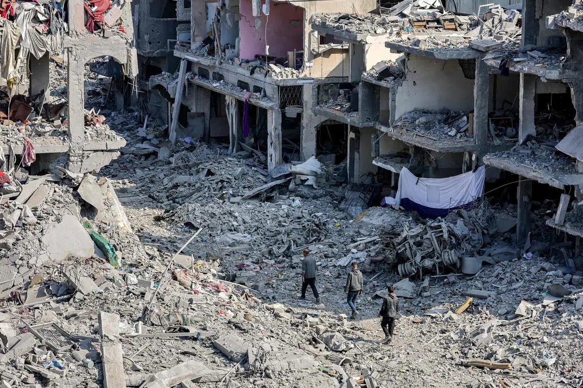 Men walk amidst the rubble past damaged and collapsed buildings in Beit Lahia in the northern Gaza Strip on Jan 20, 2025.