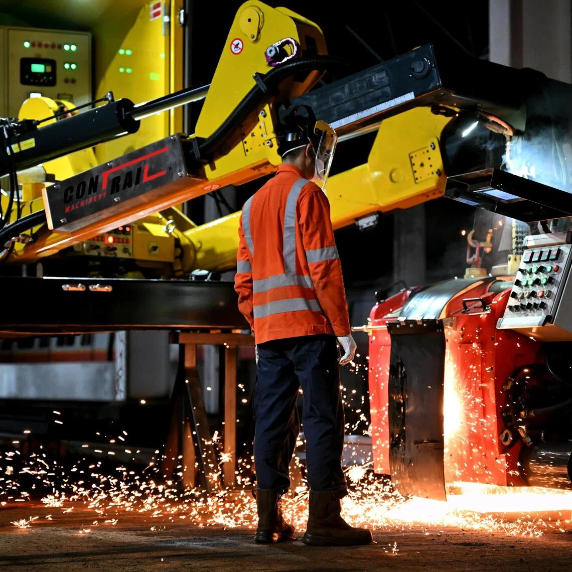 Workers using the new flash butt welding machine to press the ends of the rails together after passing an electrical current through them, to weld them together.. 