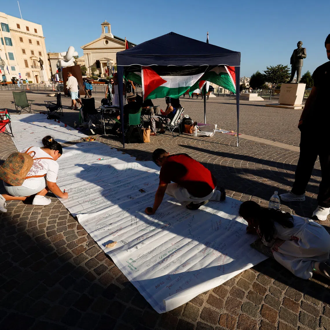 People write messages of support on a banner as activists hold a two-day protest vigil in solidarity with the victims in Gaza outside the Auberge de Castille, the office of Malta's Prime Minister Robert Abela after he announced that Malta will formally recognise the state of Palestine in the coming days, amid the ongoing conflict between Israel and Hamas, in Valletta, Malta, September 21, 2025. REUTERS/Darrin Zammit Lupi/File Photo