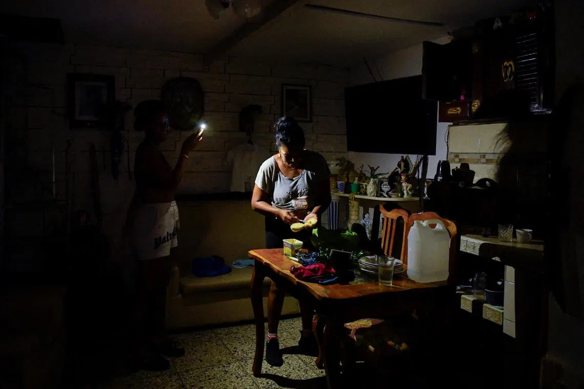 A woman prepares food with the aid of a cell phone light as Cuba is hit by an island-wide blackout, in Havana, Cuba.