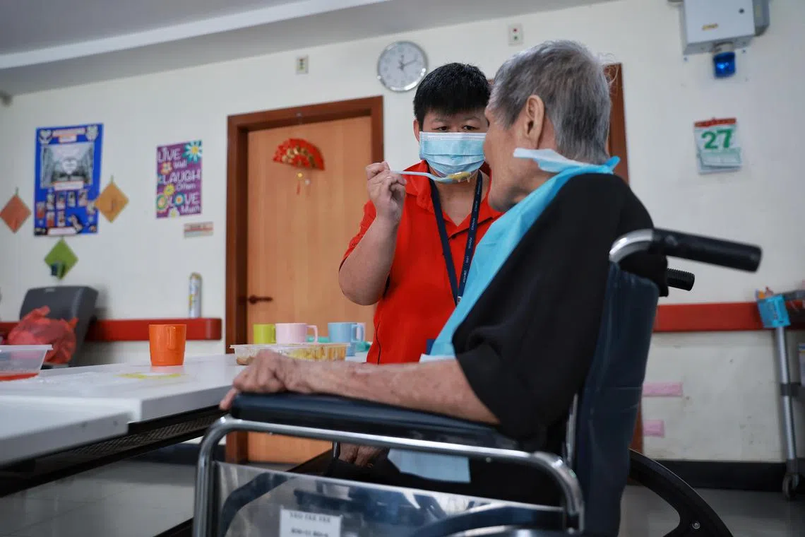 Ms Pang Jian Ting, a 34-year-old who has intellectual disability, feeding a resident during lunchtime in her role as care assistant at The Salvation Army’s Peacehaven Nursing Home on Jan 27, 2023.

People with disabilities are being hired as care assistants in nursing homes under a new tie-up between SG Enable and the Agency for Integrated Care.

Jian Ting was a General Worker at a nursery from 2012 to 2019, where she was in charge of watering plants, re-packaging items, serving customers, and performed general cleaning. She left the nursery after the business closed down.

Her next role was data entry at a social enterprise. However, during the pandemic, she was at home without any assignment. With SG Enable and its JPJS partner, MINDS, providing career advisory, job assessment and job-matching, she was matched to The Salvation Army (Peacehaven Nursing Home) as she enjoys working with the elderly. With an ageing population and a manpower crunch, we have observed many organisations in the community care sector turning to persons with disabilities as a viable talent pool too.
As a Care Assistant, she is responsible for tasks such as general cleaning, drink preparation and feeding the elderly in the home. She is able to perform her tasks independently.

She has learnt to understand the elderly she serves and their behaviour, overcoming initial challenges she faced such as when feeding the elderly. Her career growth and progress has also seen her becoming a mentor for other persons with intellectual disabilities placed in The Salvation Army (Peacehaven Nursing Home), helping them adapt to their work.