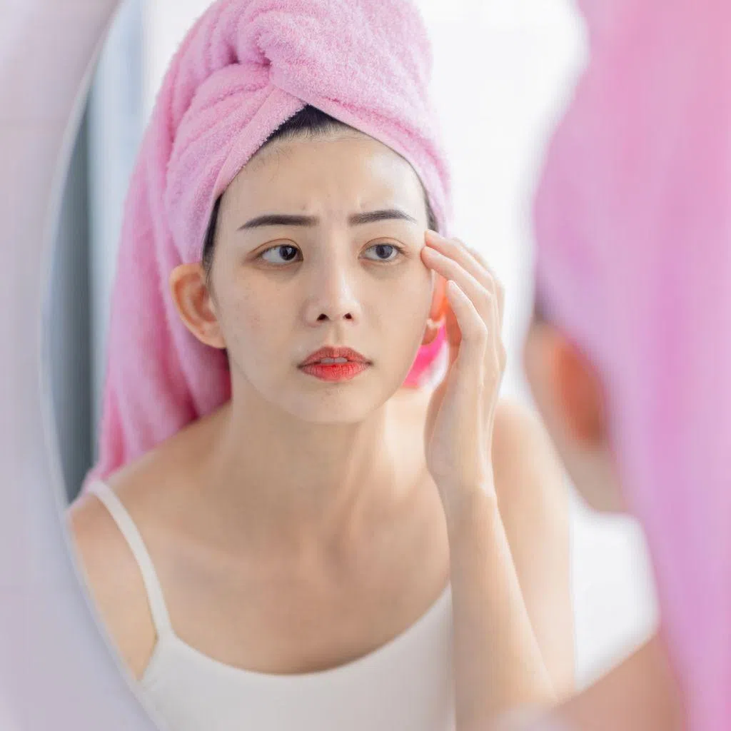 Woman looking worriedly at her eye bags in a mirror. 