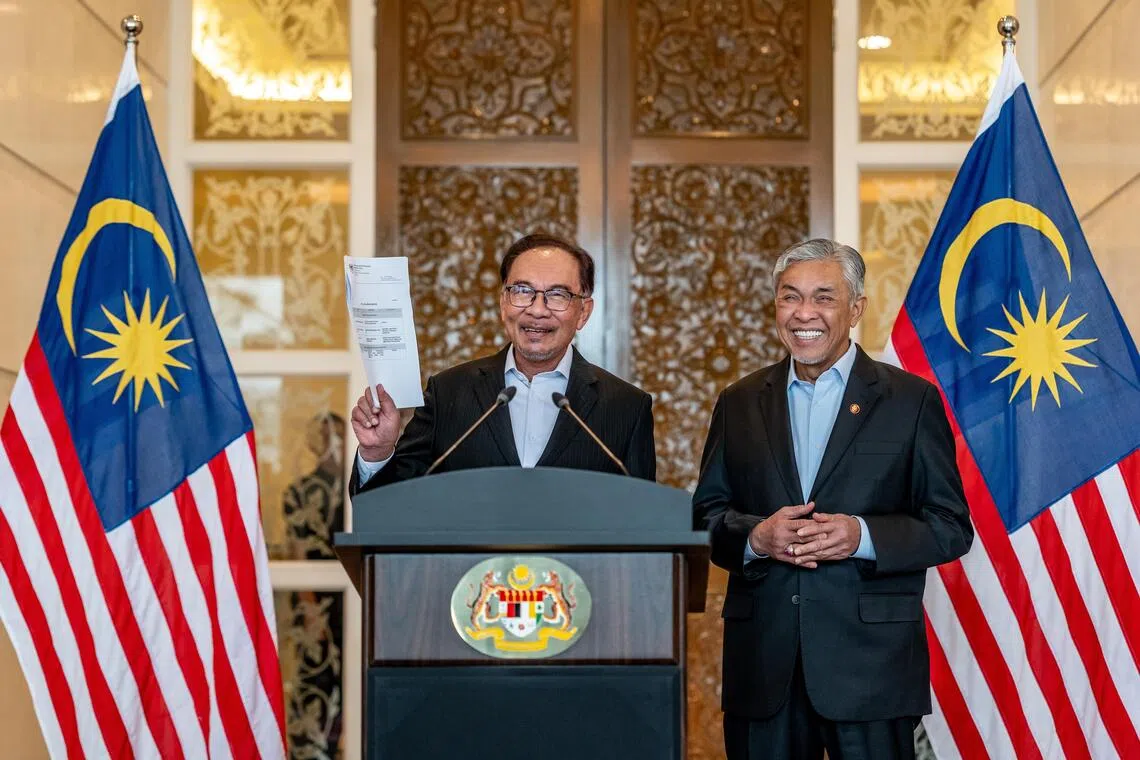 Malaysian Prime Minister Anwar Ibrahim (left) is flanked by  Deputy Prime Minister Ahmad Zahid Hamidi (right)  announcing a new Cabinet line-up of 60 people, up from 55 previously in a televised press conference on 12 December 2023.
