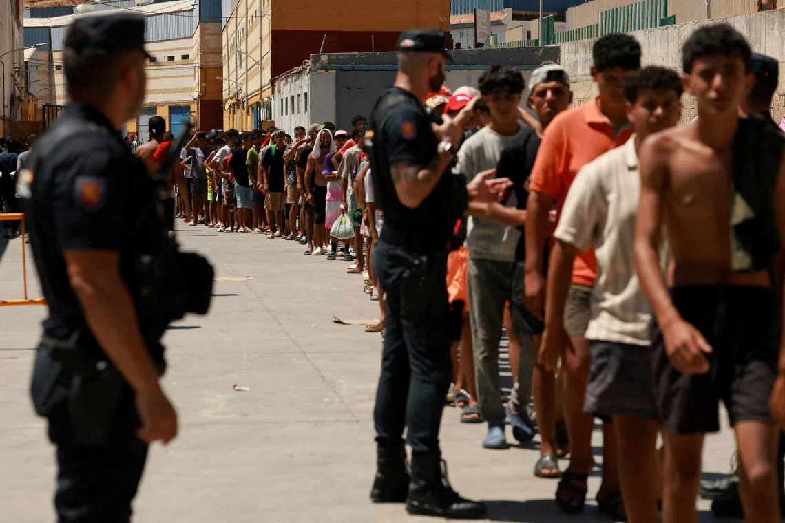 FILE PHOTO: Migrants queue to receive food staples from local NGO Media Luna Blanca in an industrial area where they are sleeping amid recent mass crossings by migrants on foot and by sea from Morocco into the Spanish territory, in Ceuta, Spain, August 6, 2026. REUTERS/Violeta Santos Moura/File Photo