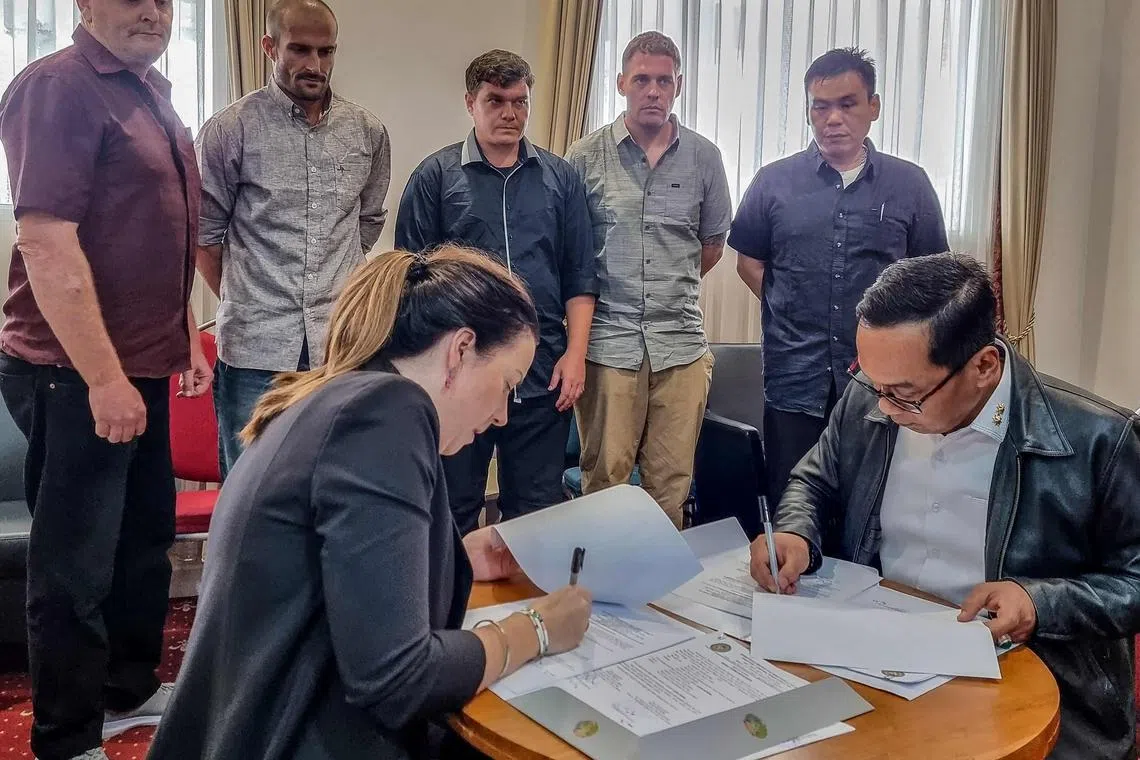 Five 'Bali Nine' convicts look on as Indonesia's director of prisoner development Erwedi Supriyatno (front right) and Australian representative Lauren Richardson (front left) sign a transfer agreement.