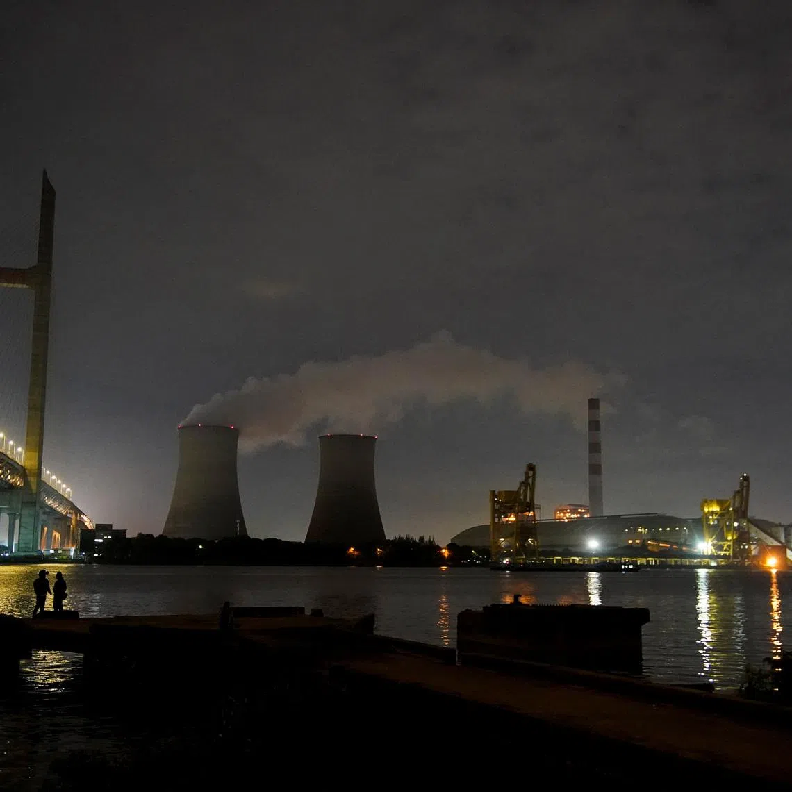 FILE PHOTO: People stand on a bank of the Huangpu river near a coal-fired power plant in Shanghai, China, October 14, 2021. REUTERS/Aly Song