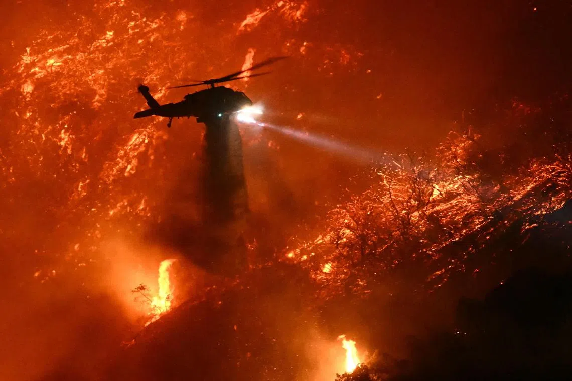 A fire fighting helicopter drops water as the Palisades fire grows near the Mandeville Canyon neighborhood and Encino, California, on January 11, 2025. The Palisades Fire, the largest of the Los Angeles fires, spread toward previously untouched neighborhoods January 11, forcing new evacuations and dimming hopes that the disaster was coming under control. Across the city, at least 11 people have died as multiple fires have ripped through residential areas since January 7, razing thousands of homes in destruction that US President Joe Biden likened to a "war scene." (Photo by Patrick T. Fallon / AFP)