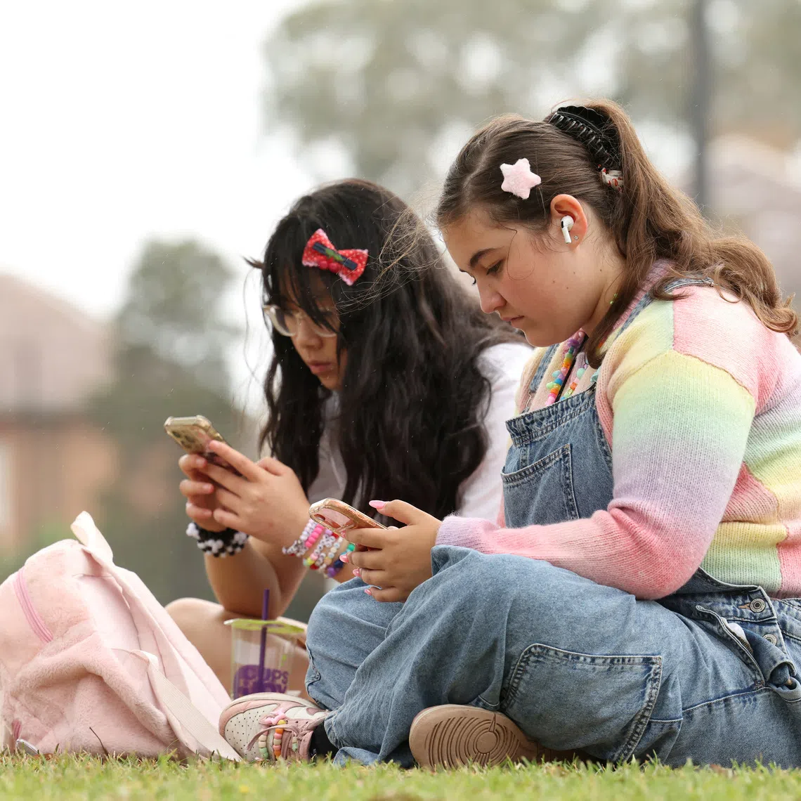 Annie Wang, 14, and Ayris Tolson, 15, use their mobile phones, ahead of Australia’s social media ban for users under 16, which is scheduled to take effect on December 10, in Sydney, Australia, November 22, 2025. REUTERS/Hollie Adams