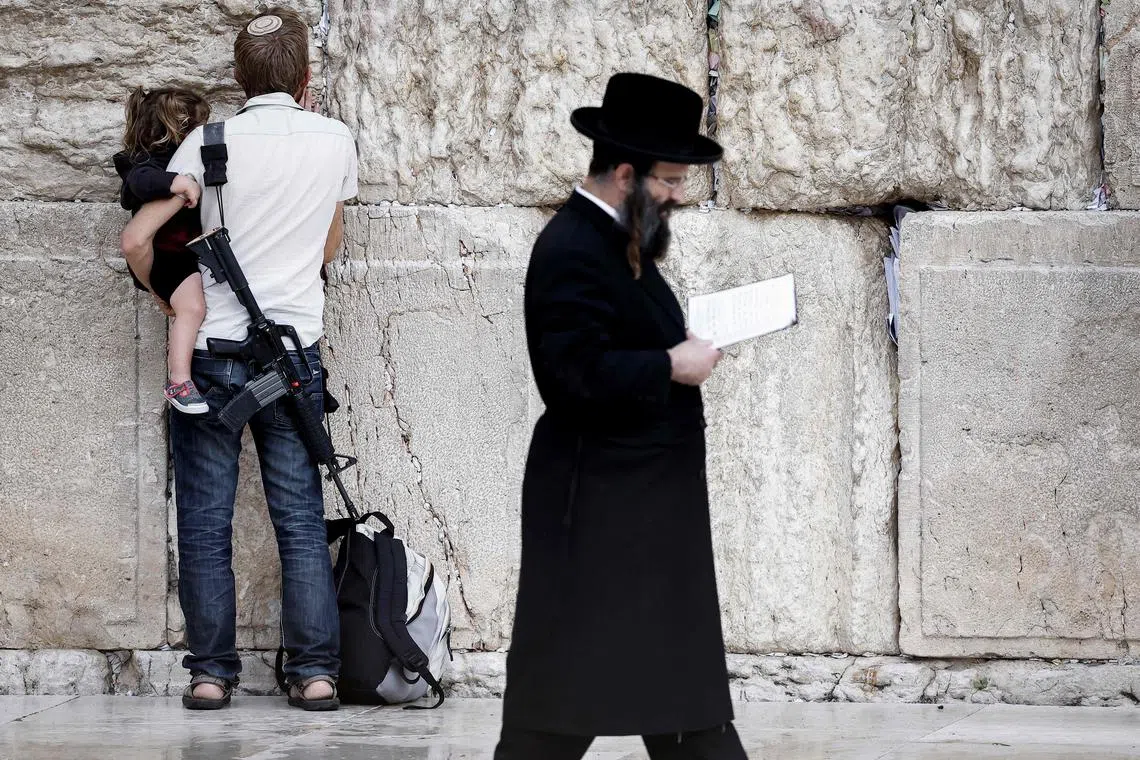 An armed Jewish man holding a child as he prays at the Western Wall, the last remaining vestige of the Second Temple, in Jerusalem's Old City on Nov 12, 2023.