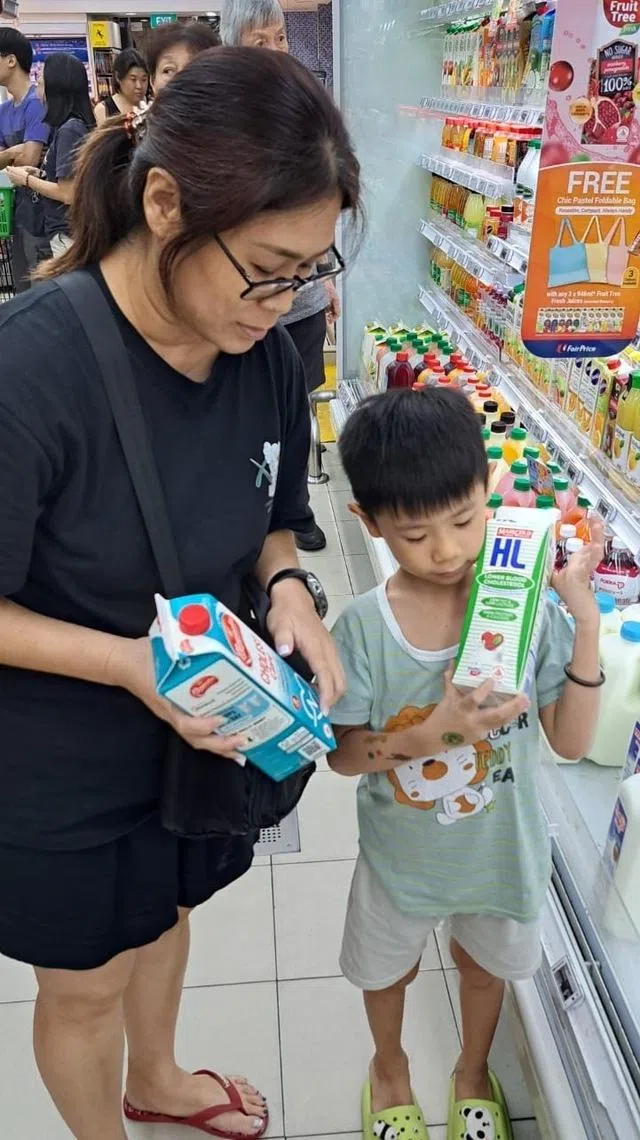 Isaac Yap from My First Skool looking at the Healthier Choice symbol with his mother standing next to FairPrice supermarket’s fresh milk chiller
