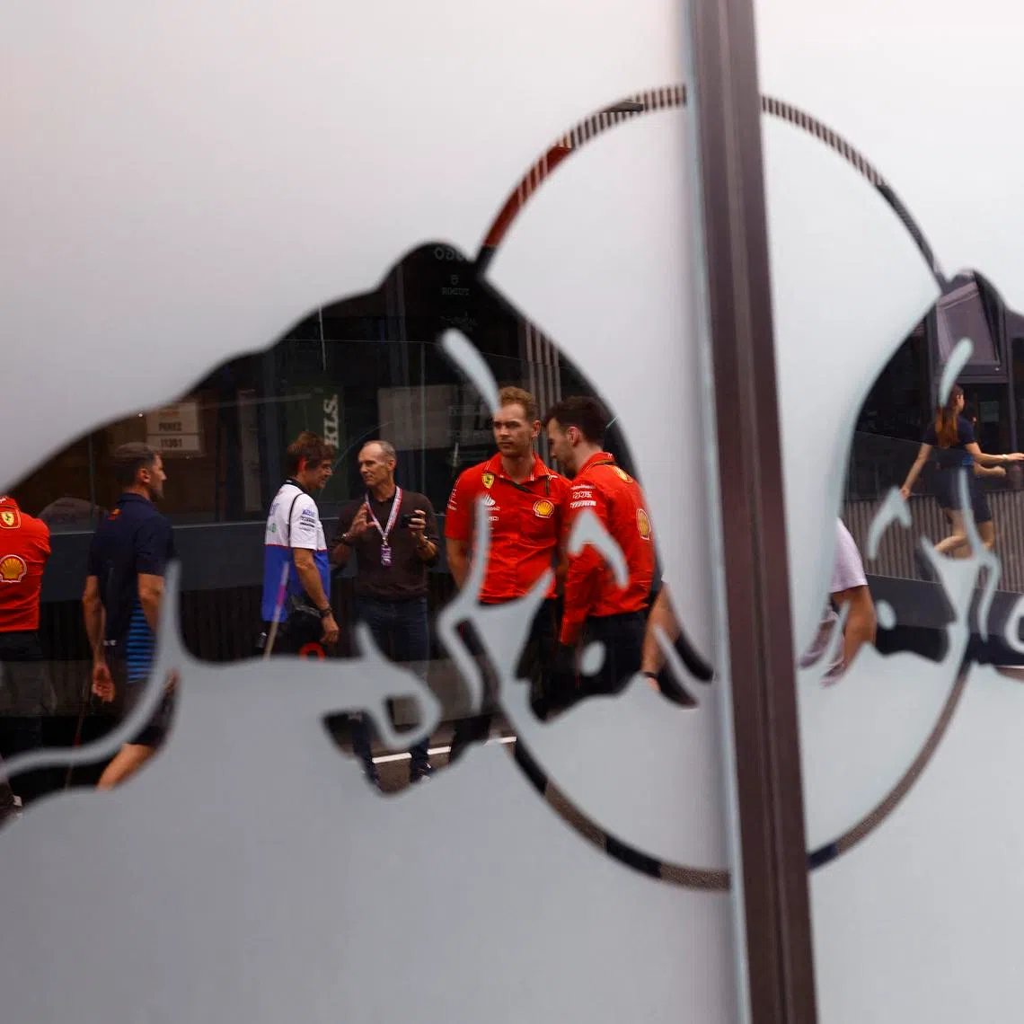 Formula One F1 - Spanish Grand Prix - Circuit de Barcelona-Catalunya, Barcelona, Spain - June 20, 2024 People in the paddock are seen in the reflection of a Red Bull logo ahead of the Spanish Grand Prix REUTERS/Susana Vera