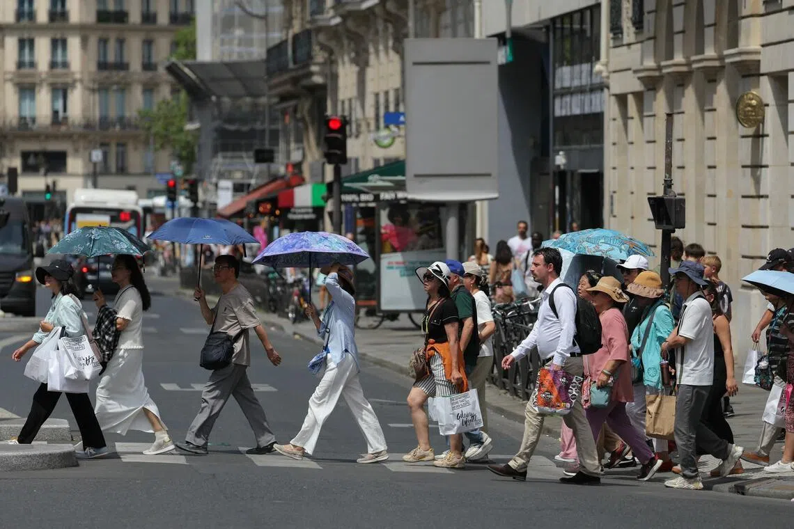 Tourists protecting themselves from the sun under umbrellas while crossing a street in Paris on June 23.
