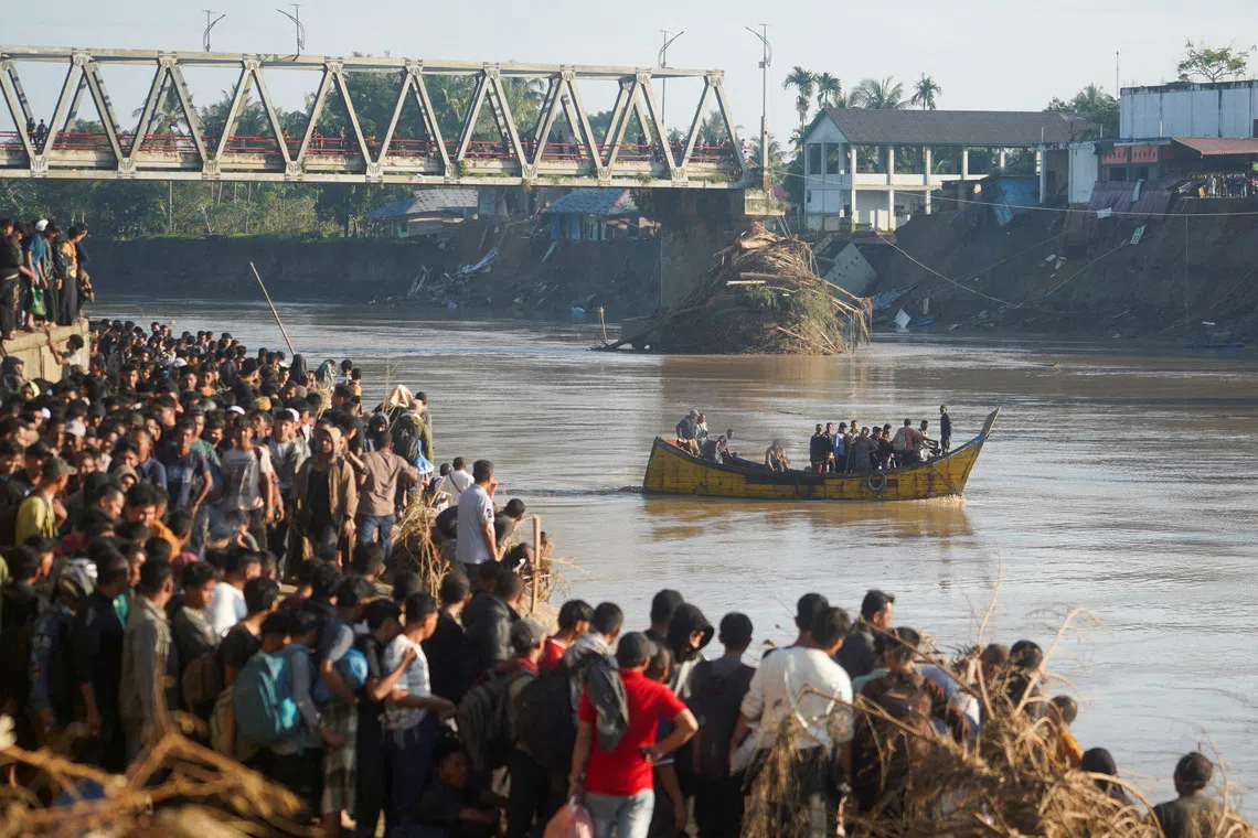 People ride a wooden boat to cross a river as others wait, at an area hit by deadly flash floods following heavy rains in Bireuen Regency, Aceh, Indonesia, November 29, 2025. REUTERS/Hendri