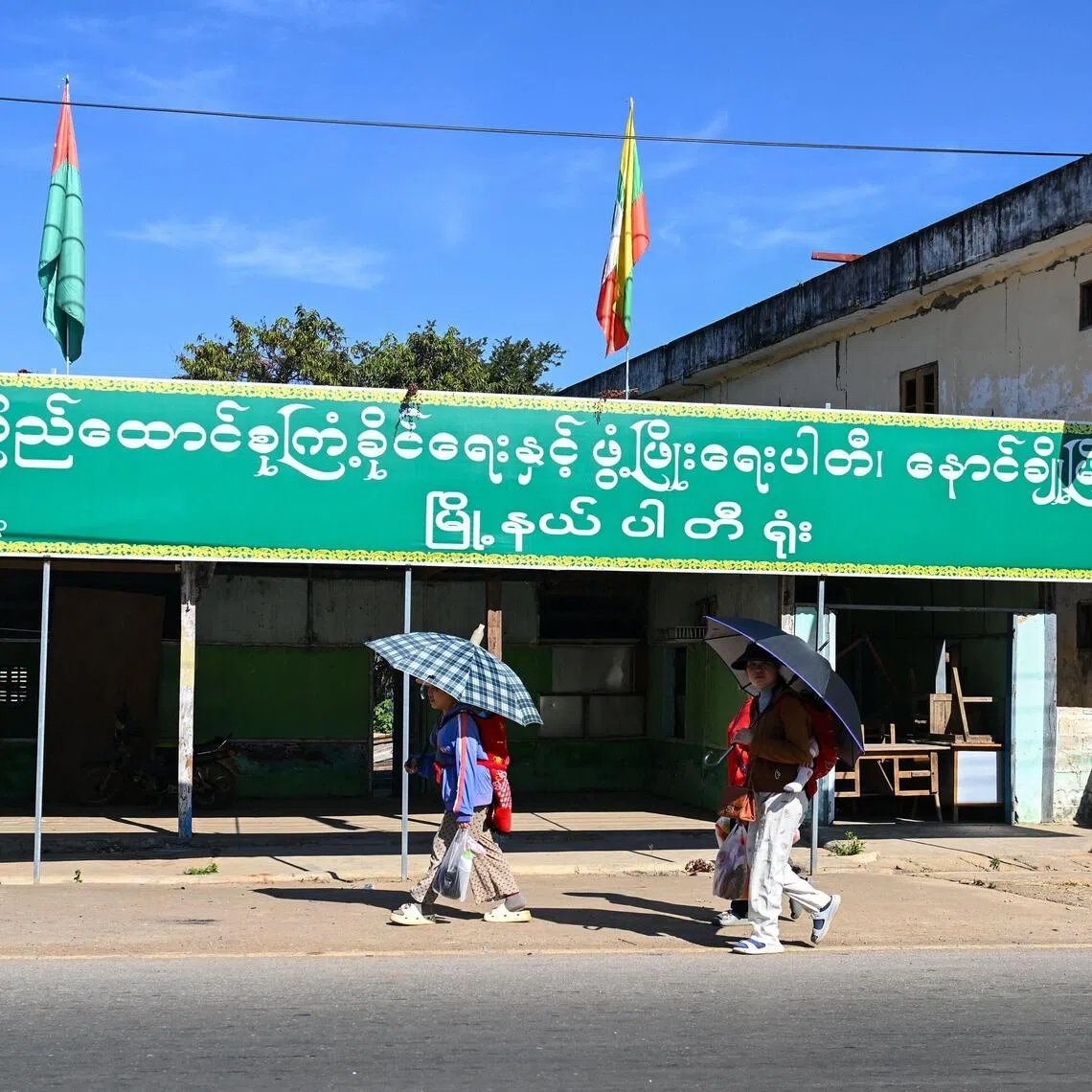 People walk past an election campaign billboard ahead of Myanmar's general election in Nawnghkio in Myanmar’s northern Shan State, on Dec 9, 2025.