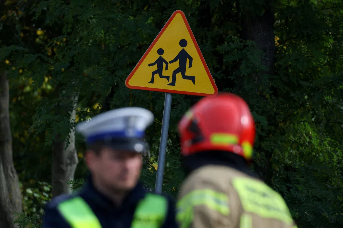 A police officer and a fire fighter stand near a road sign as they work at the site of a deadly attack at a school by a 15-year-old former pupil, in Leszczydol-Nowiny, Wyszkow County, northeast of Warsaw, Poland, October 8, 2026. REUTERS/Kacper Pempel
