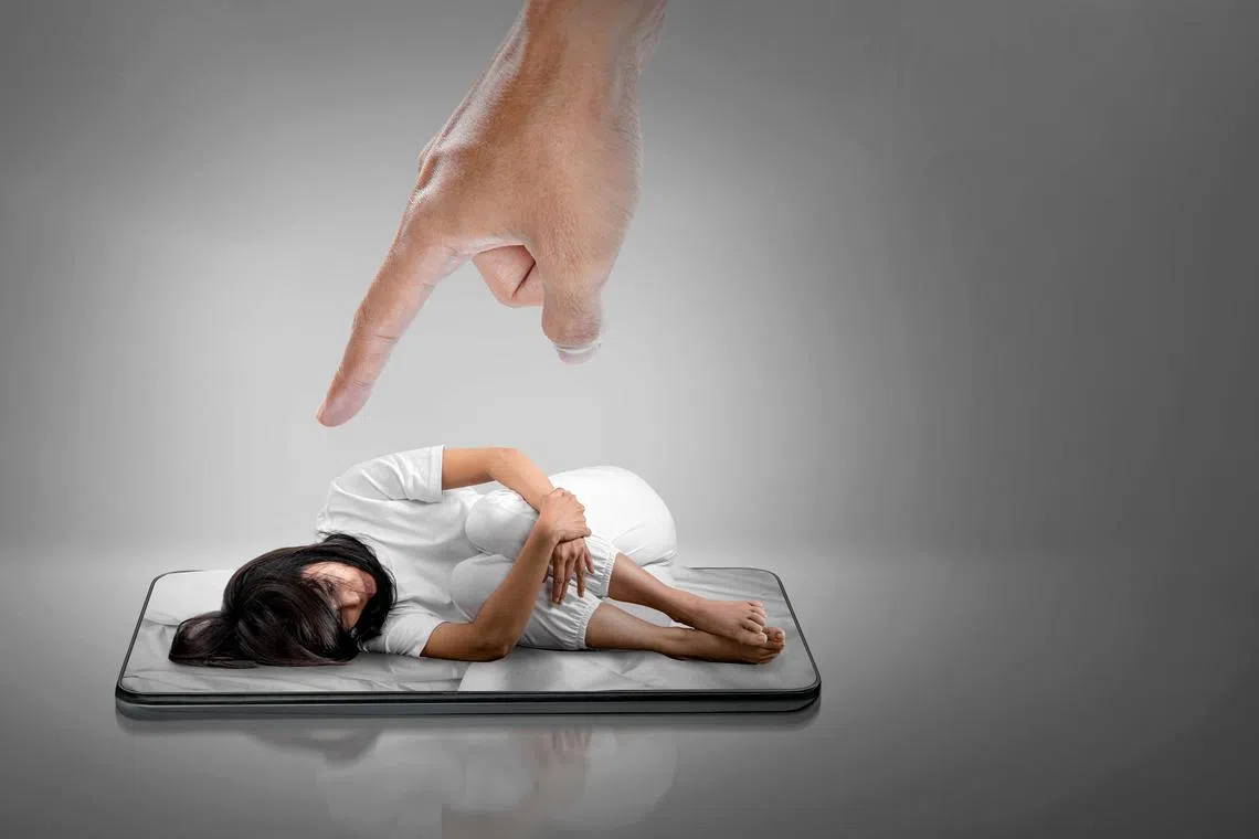 The depressed woman is lying on the mobile phone screen with a judgmental hand pointing at her. Cyberbullying Concept