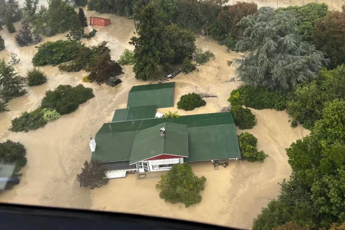 A handout photo taken and received on Feb 14, 2023, from the New Zealand Defence Force shows stranded people preparing to be air lifted from their rooftop by a military helicopter in the Esk Valley, near the North Island city of Napier. 
