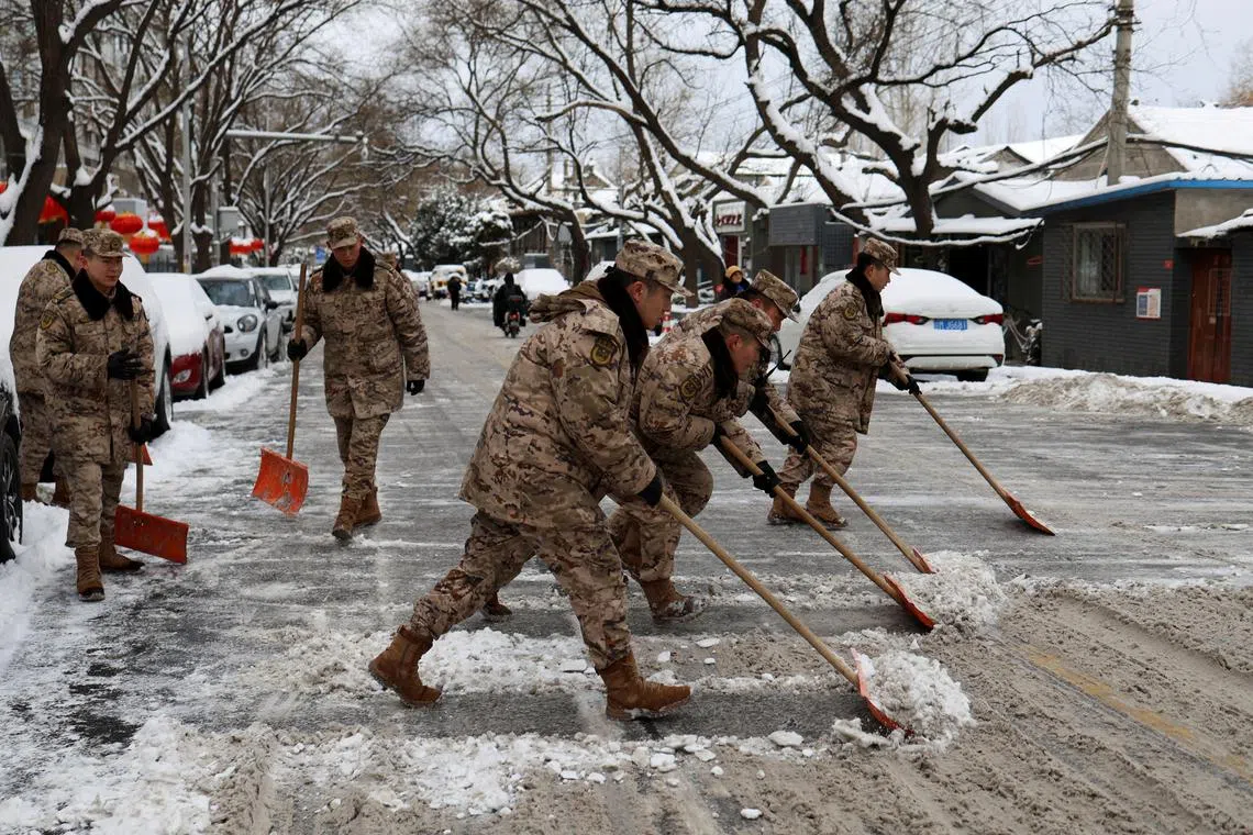 FILE PHOTO: Paramilitary police officers remove snow from a road following snowfall in Beijing, China February 21, 2024. REUTERS/Florence Lo/File Photo