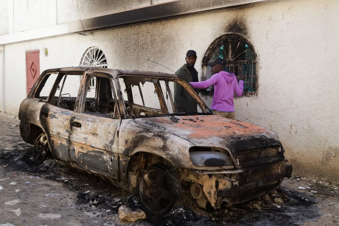 People stand next to a burned car after a fatal overnight raid by an armed gang, on the outskirts of Port-au-Prince, in Kenscoff, Haiti, August 24, 2026. REUTERS/Fildor Pq Egeder