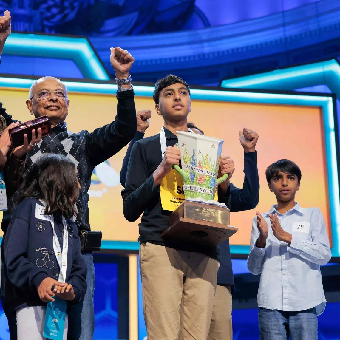 Shrey Parikh, 14, holding a trophy and celebrating with family after winning the 2026 Scripps National Spelling Bee on May 28.