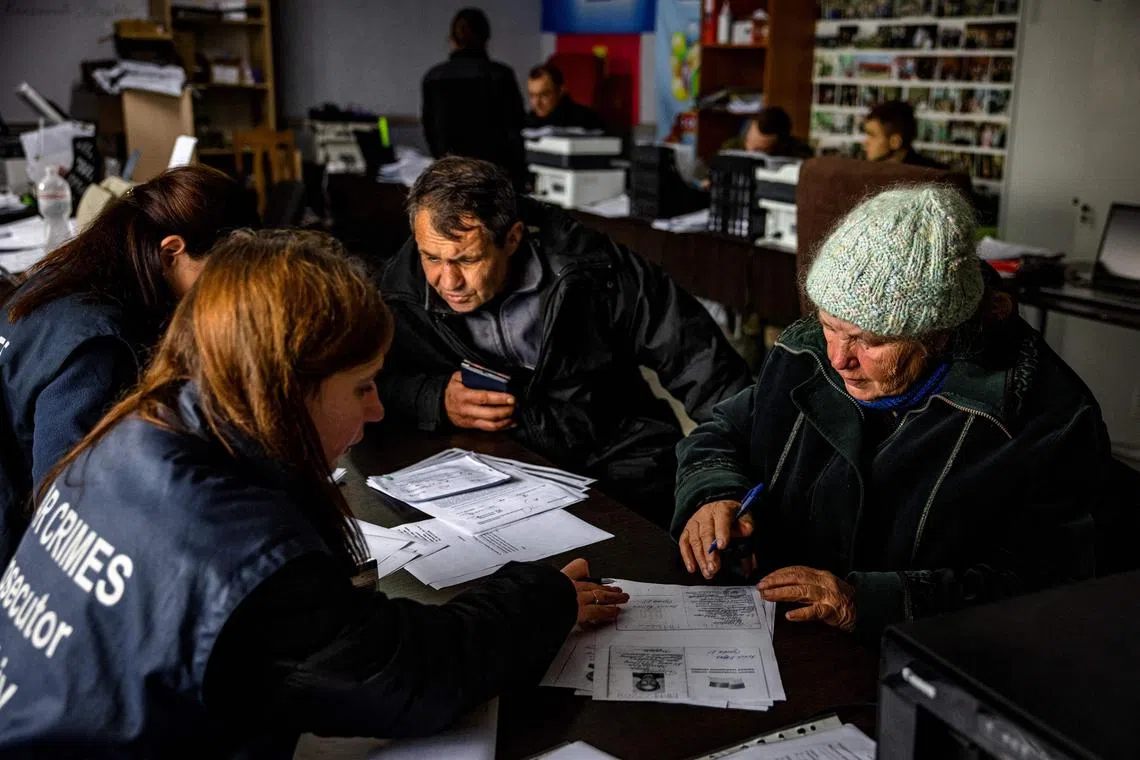 Ukrainian Anna Sukhova (right), 78, fills out paperwork for war crimes investigators to submit her DNA for the identification of her brother,  in the town of Izyum, in Ukraine's Kharkiv region, on Nov 4, 2022.