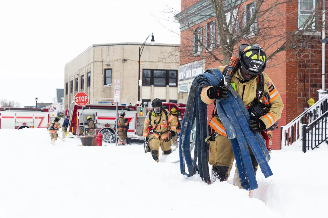 Firefighters carry equipment as they respond to a fire on a snow covered street on Christmas Day in Buffalo, N.Y., Dec. 25, 2022. The death toll from the violent snowstorm that has blanketed parts of Western New York in nearly four feet of snow rose to seven people overnight. (Jalen Wright/The New York Times)