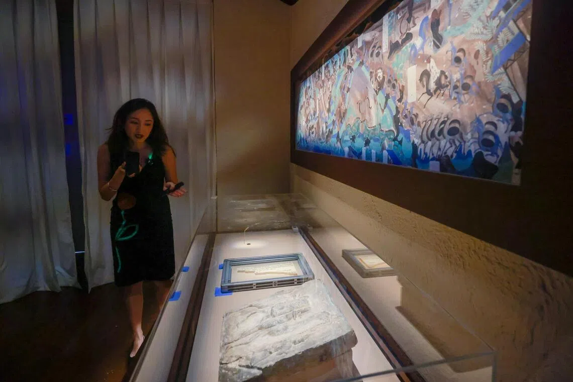 Curator Louise Lui in front of a painting from the caves that includes medallions of horoscopes from the West.