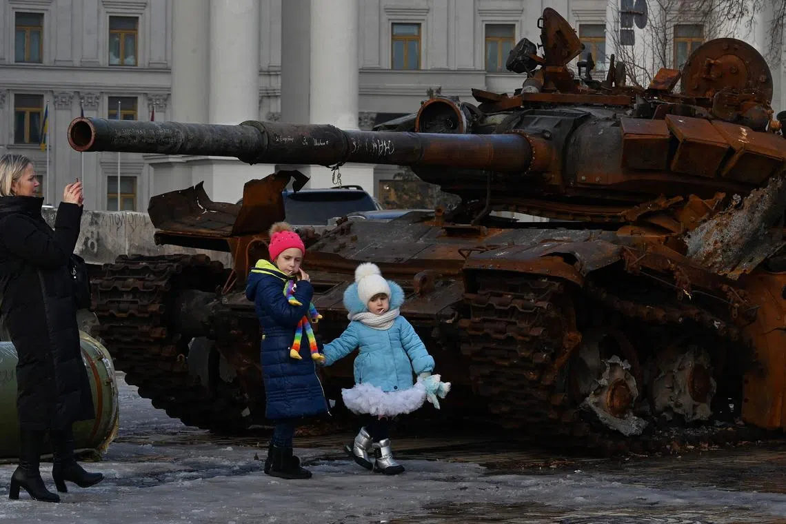 A woman takes a photograph of children walking past a tank in Kyiv, on Dec 23, 2022.